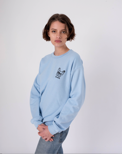 Side view of light blue crewneck sweatshirt with embroidery of french bulldog face on the  left of the chest on woman in jeans