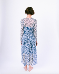 Back view of long sleeve blue and white floral a-line dress with mesh overlay over slip dress on woman